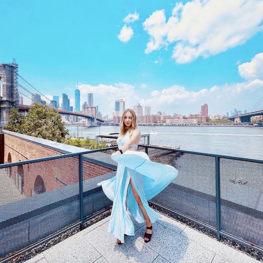 Rena twirling in a blue dress on a rooftop by the Brooklyn Bridge