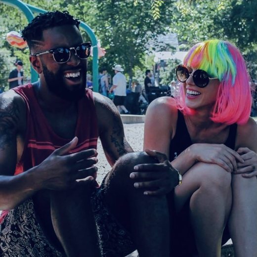 Rena in a rainbow wig laughing with a friend at a festival